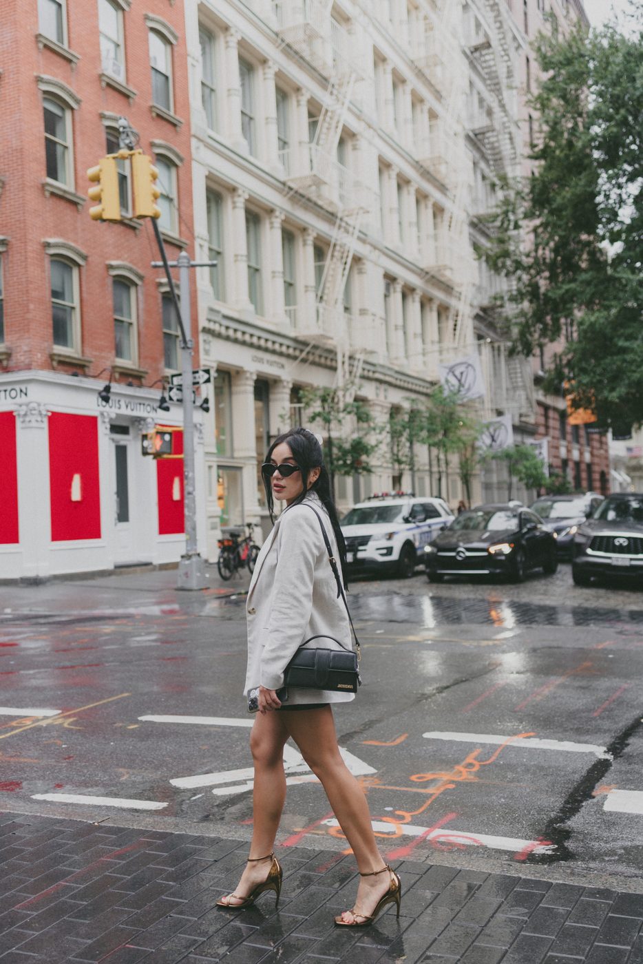 Woman in a linen blazer and sunglasses crossing a wet SoHo street
